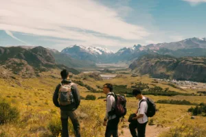 Three hikers observe a vast mountain valley landscape.
